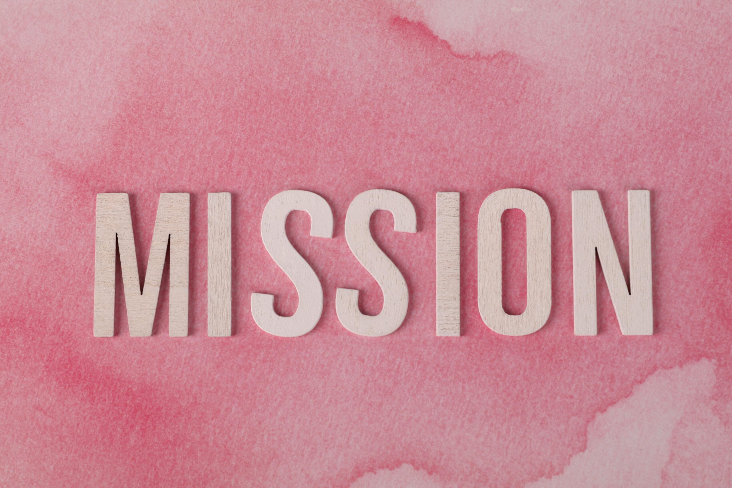Wooden letters spelling 'MISSION' on a soft pink watercolor background.